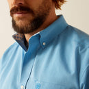 Men's Ariat long sleeve wrinkle free shirt in Blue. Close up view of button down collar showing contrast pattern in neck band and Ariat logo shield on left chest pocket. 