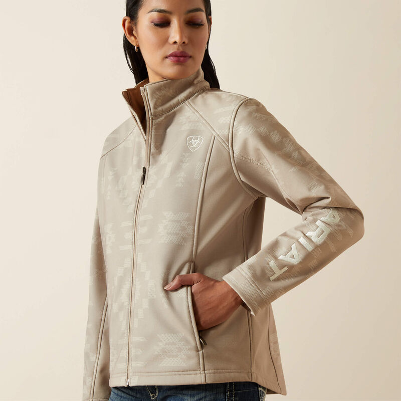 Women's Ariat softshell logo jacket in Tan Southwest Cross Stitch. This jacket features a bold Ariat logo on left sleeve. Close up of logo on left sleeve and left chest, also showing pockets. 