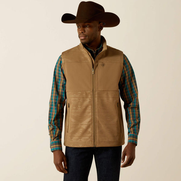 Men's Ariat khaki vesty with full front zipper with wind stop lining, left chest Ariat logo, zippered hand pockets, and standing collar. Shows solid color chest and with tonal geometric print on yoke and lower body . Hits mid hip. Front view.