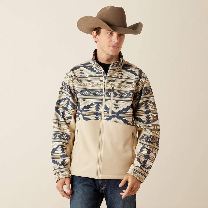Men's Ariat Softshell jacket in White Pepper Southwest. This jacket has a solid beige bottom and a Southwestern pattern on the top made of blue and browns. It has a zippered close and a bold Ariat logo on left sleeve. 