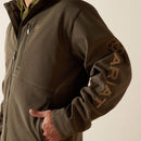 Ariat men's softshell jacket in Earth Green Heather. This jacket features a bold Ariat logo on the left sleeve in brown. Close up of left sleeve showing Ariat logo in brown. 