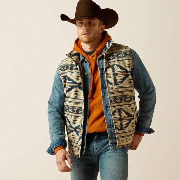 Men's Ariat soft shell azted print weather resistant vest. Has full front zipper, standing collar, left chest vertical zippered phone pocket with Ariat logo, slash zippered hand pockets.  Hits mid hip. Front view.