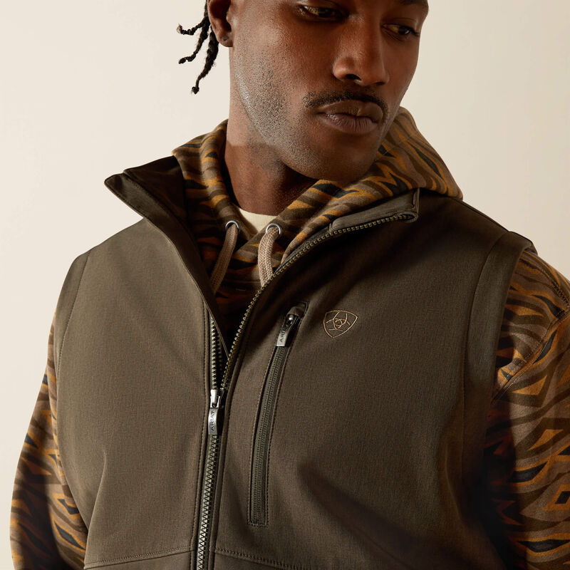 Men's Ariat dark green heather vest front closeup showing standing collar, front zipper, zippered left chest outside pocket. Sleeveless arm openings hemmed.