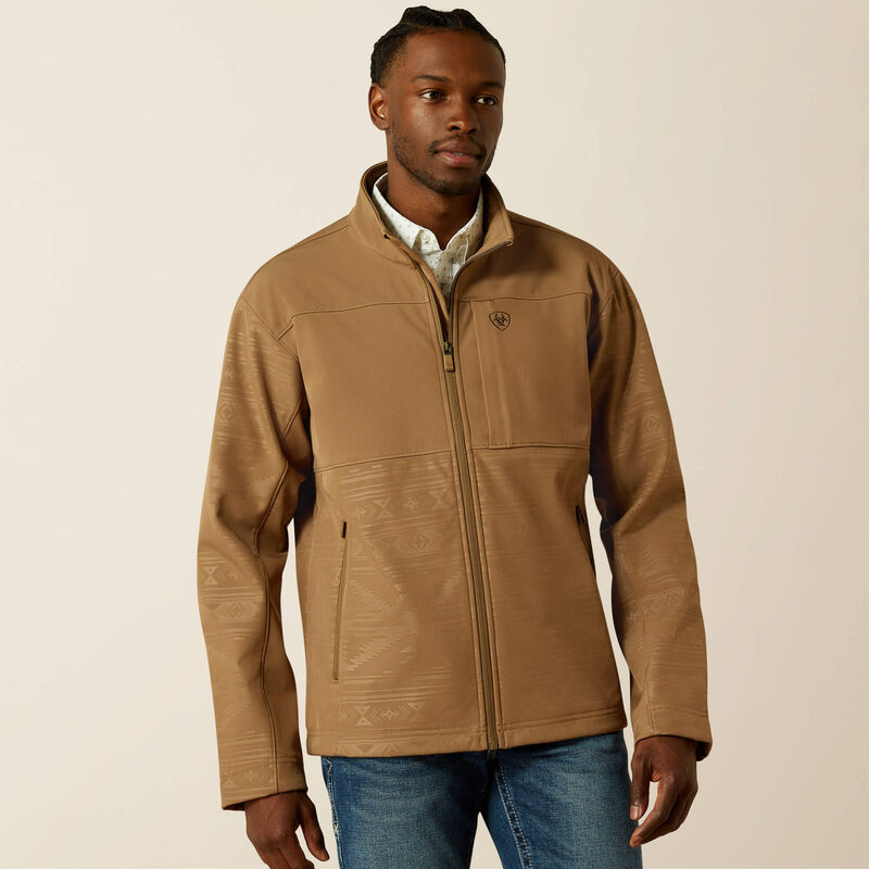 Men's Ariat khaki jacket with full front zipper with wind stop lining, left chest Ariat logo, zippered hand pockets, and standing collar. Shows solid yoke and chest with tonal geometric lower body and sleeves. Hits upper thigh. Front view.