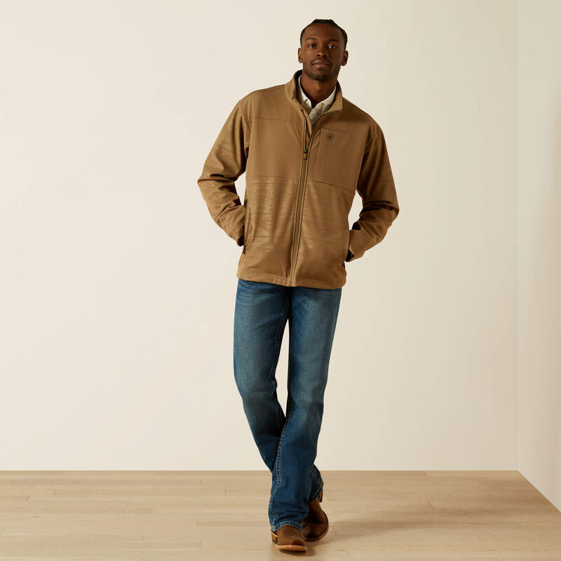 Men's Ariat khaki jacket with full front zipper with wind stop lining, left chest Ariat logo, zippered hand pockets, and standing collar. Shows solid yoke and chest with tonal geometric lower body and sleeves. Hits upper thigh. Full front body view.