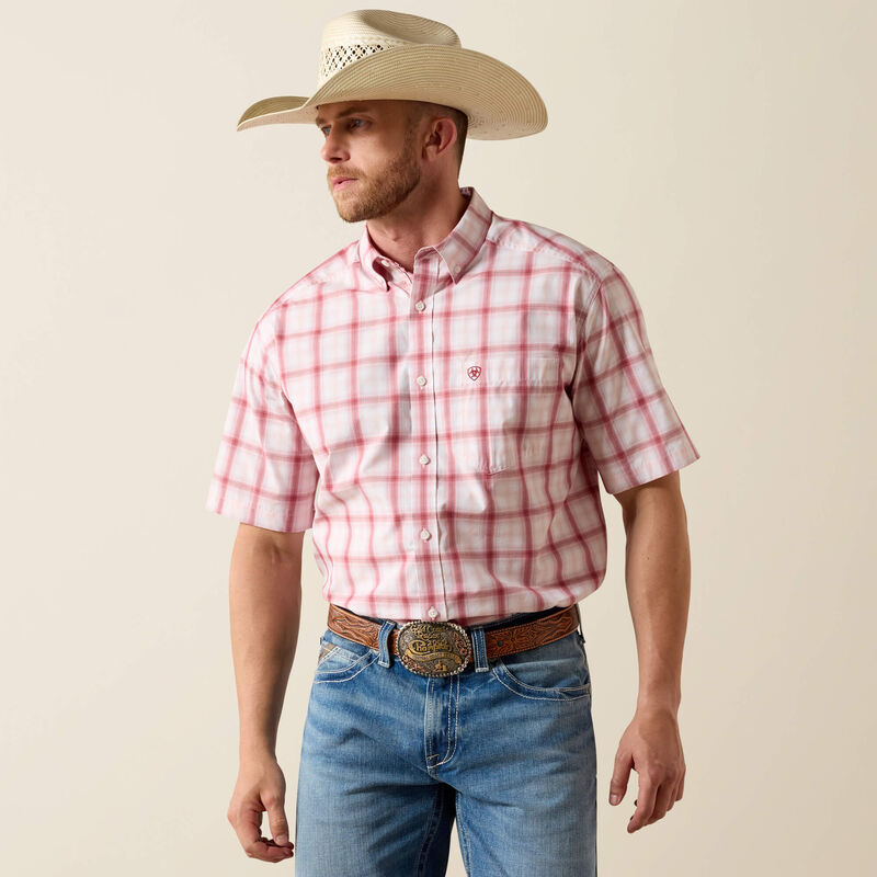 Man wearing a red plaid shirt, blue jeans, and a cowboy hat against a beige background