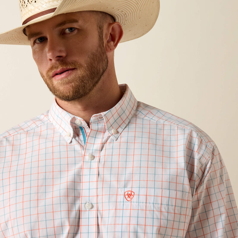 Men's Ariat long sleeve team logo shirt in white plaid, a orange and blue plaid. It features a button down collar and a orange Ariat shield logo on the left chest pocket. Close up of front showing button down collar and Ariat shield logo on pocket details. 