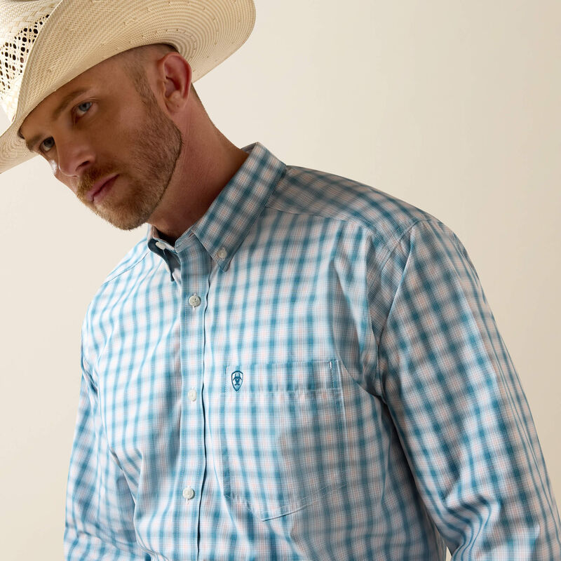 Men's Ariat long sleeve shirt in Corsair Plaid, a blue plaid pattern. Close up front view showing button down collar and Ariat logo shield on left chest pocket. 