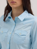 Close-up of a woman wearing a long sleeve wrangler shirt in cool blue with a spread collar, button front placket, and button flap pockets.