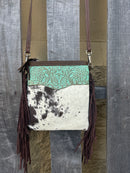This cowhide and leather crossbody bag has fringe side details and a embossed Turquoise panel along the top front of the bag. 
