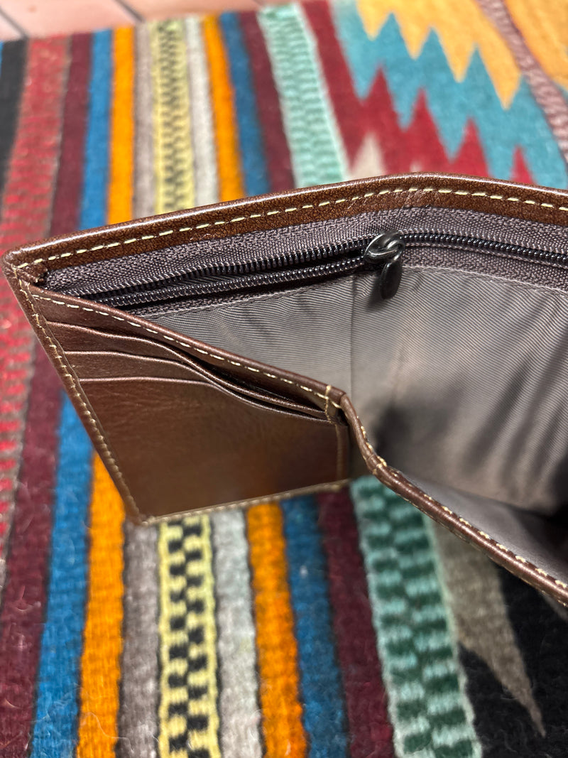 This brown leather trifold wallet has a stitching pattern along the top. Close up view of cash slots showing zip closure. 