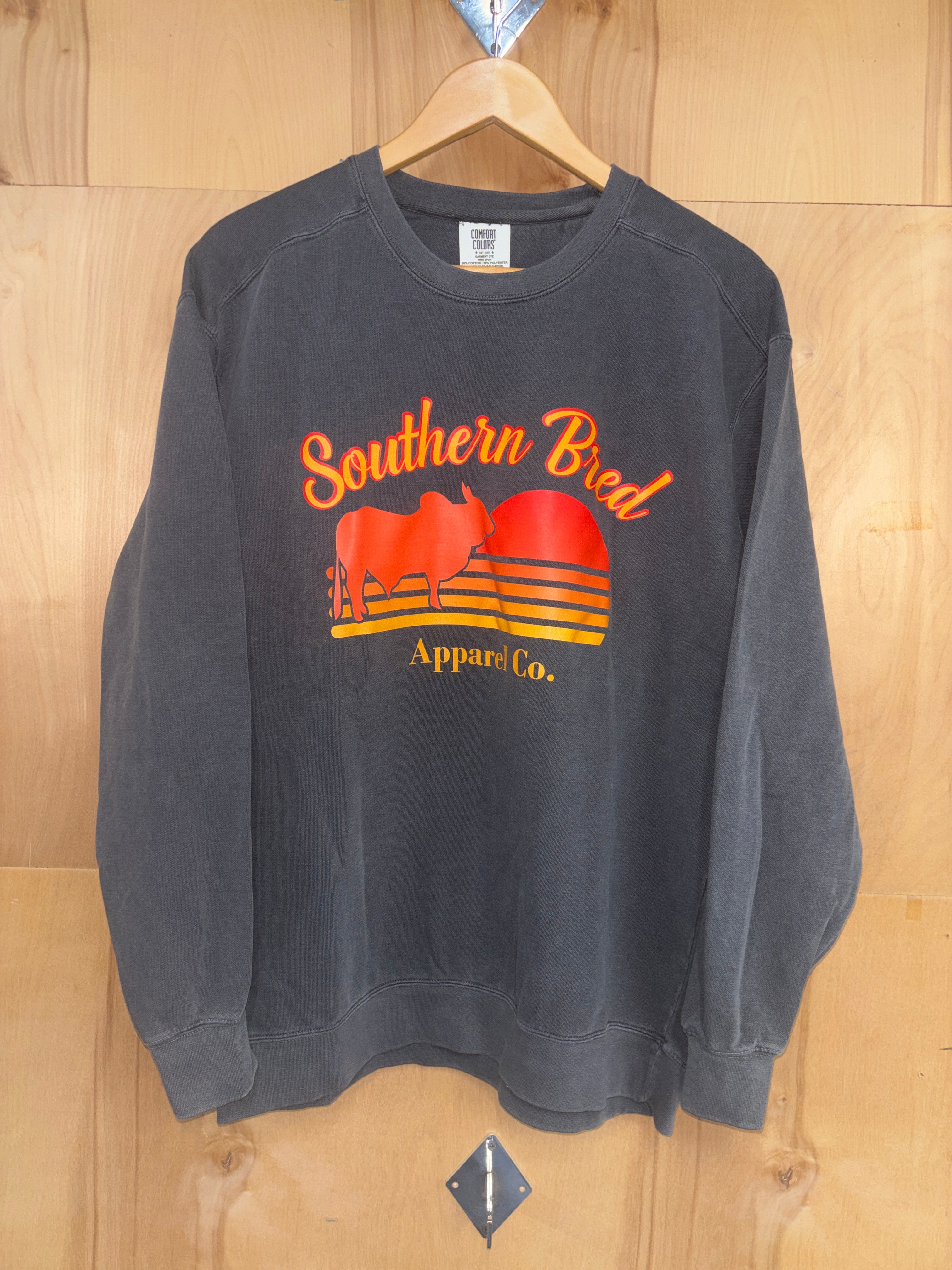 Southern Bred Apparel Company crewneck Comfort Colors brand sweatshirt in Pepper. This grey sweatshirt features a front graphic print of "Southern Bred Apparel Co." and a outline of a Brahman Bull. 