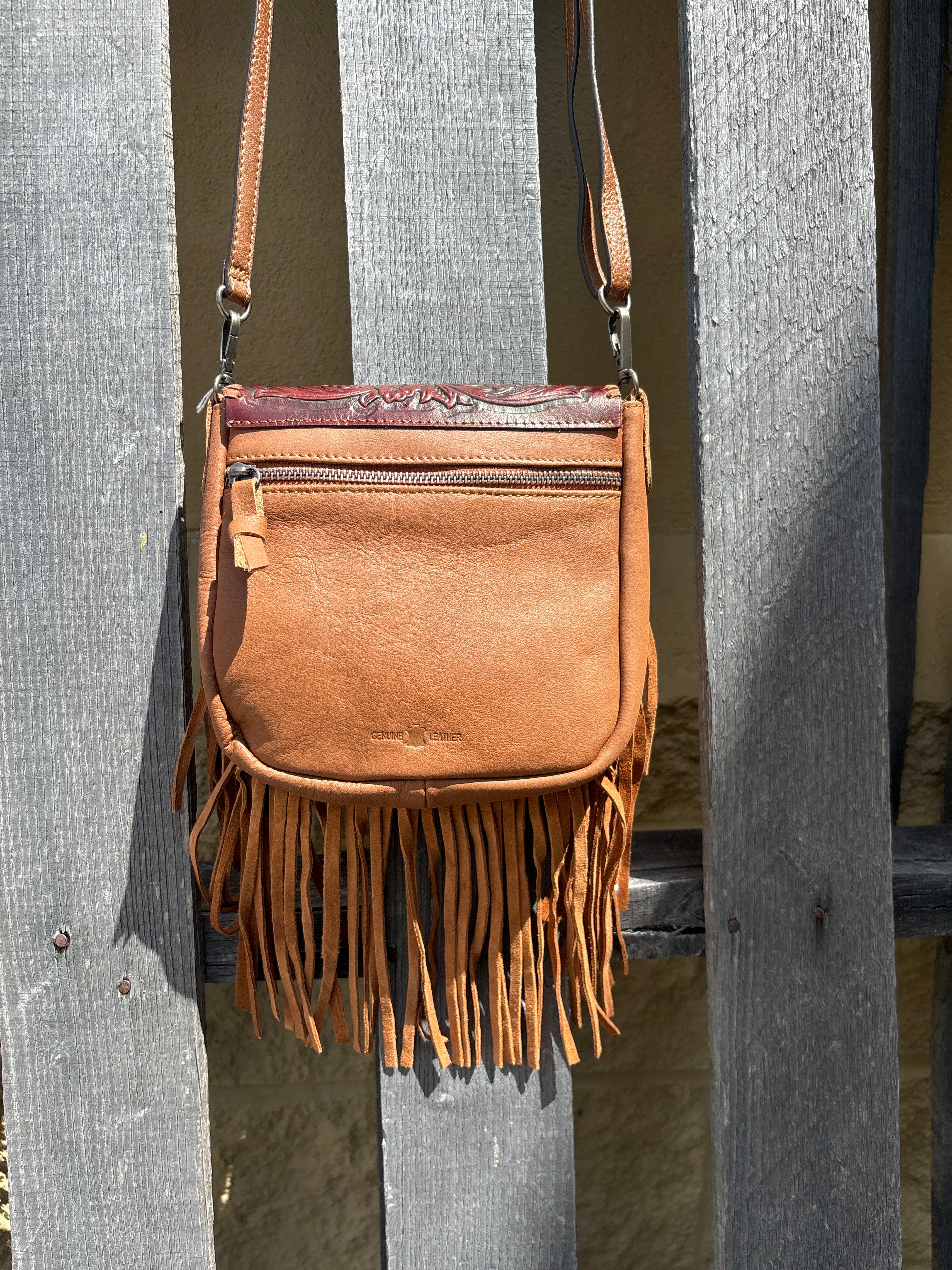 This Brown leather crossbody bag features fringe sides and a tooled flap with a whipstitch border. It has a removable and adjustable shoulder strap.  Rear view showing pocket that zips closed. 