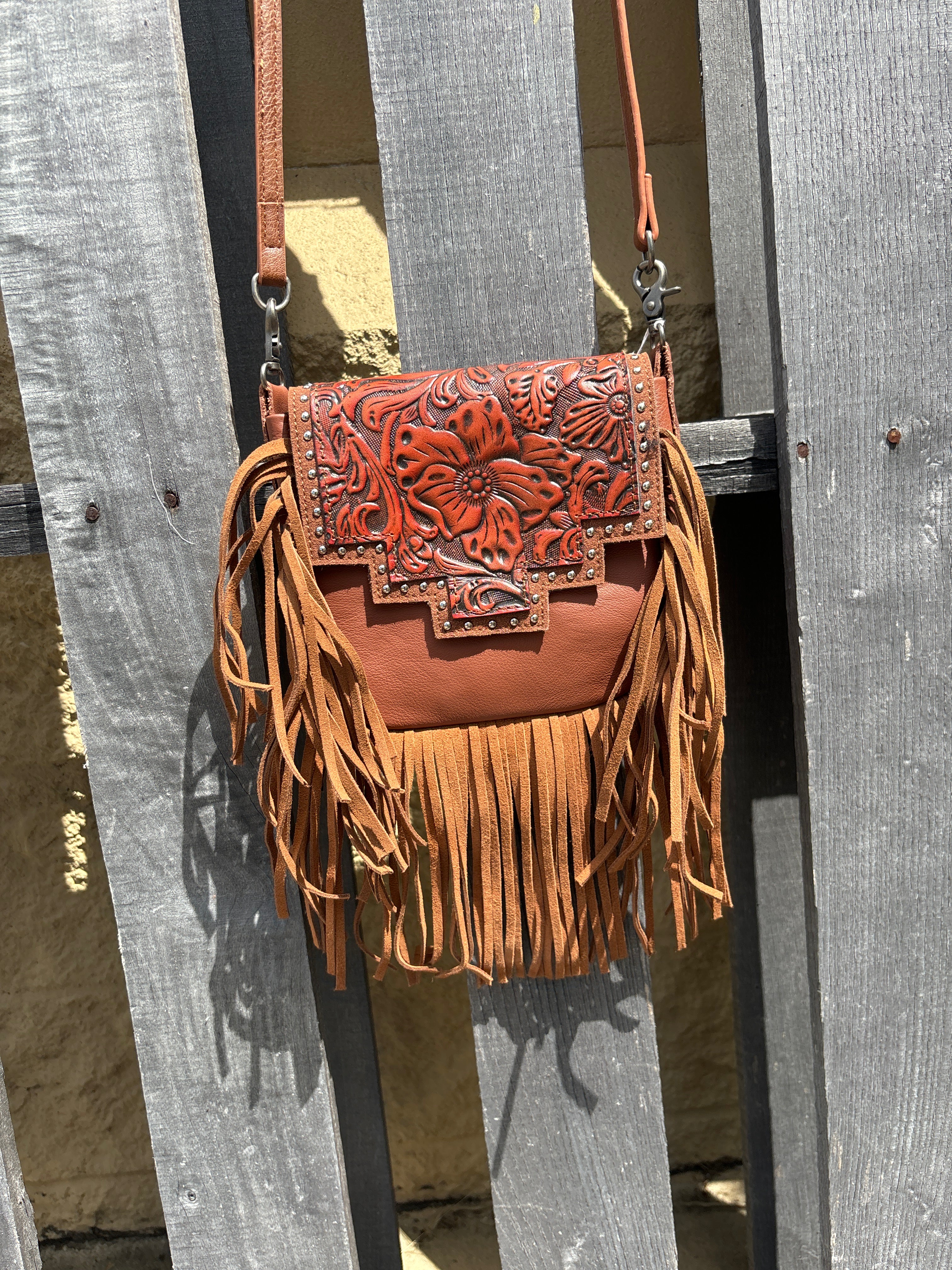 Brown leather crossbody bag with a fringe sides and a tooled design on the flap. Front View