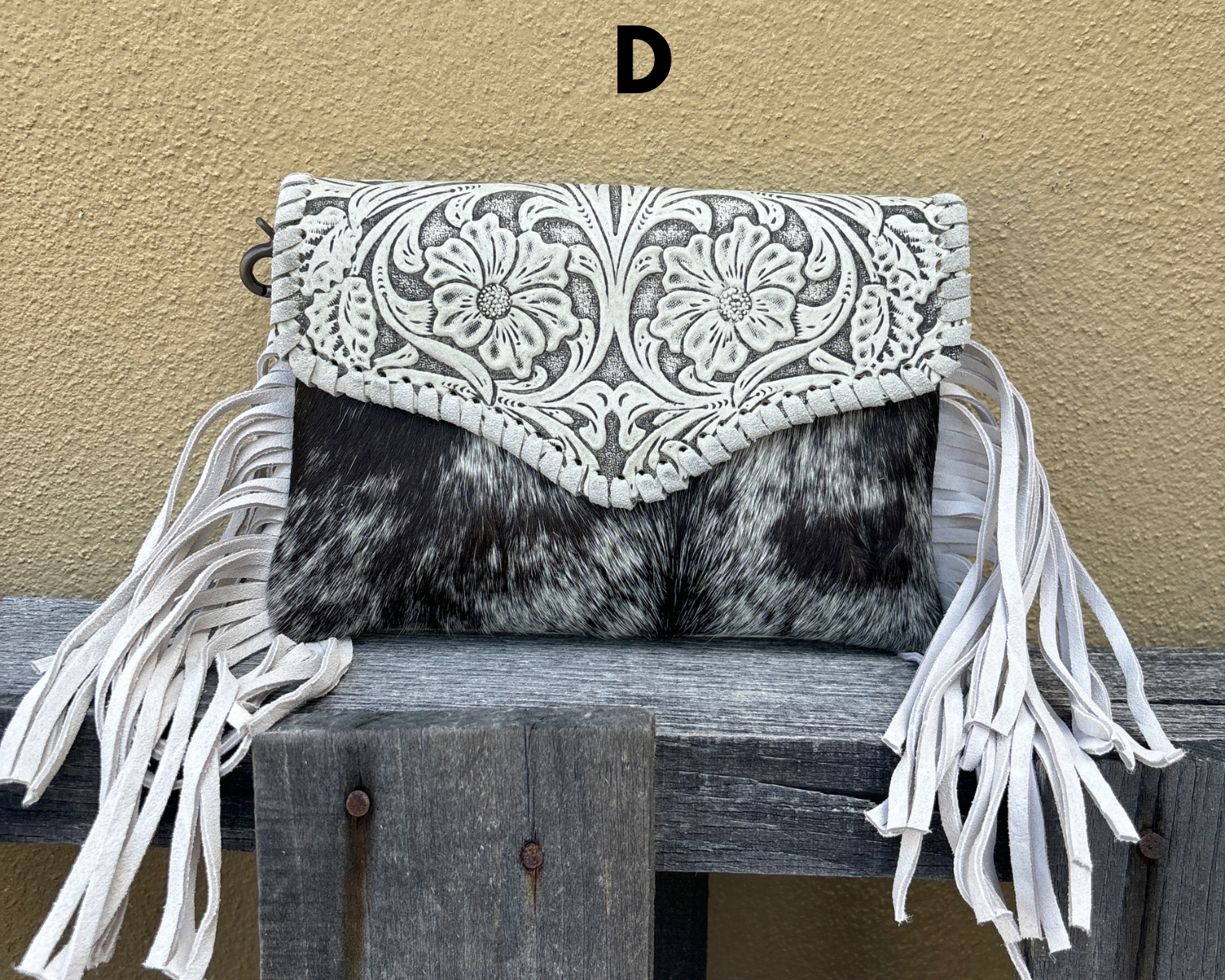 Clutch bag with white fringe and intricate design on a wooden surface against a beige wall.