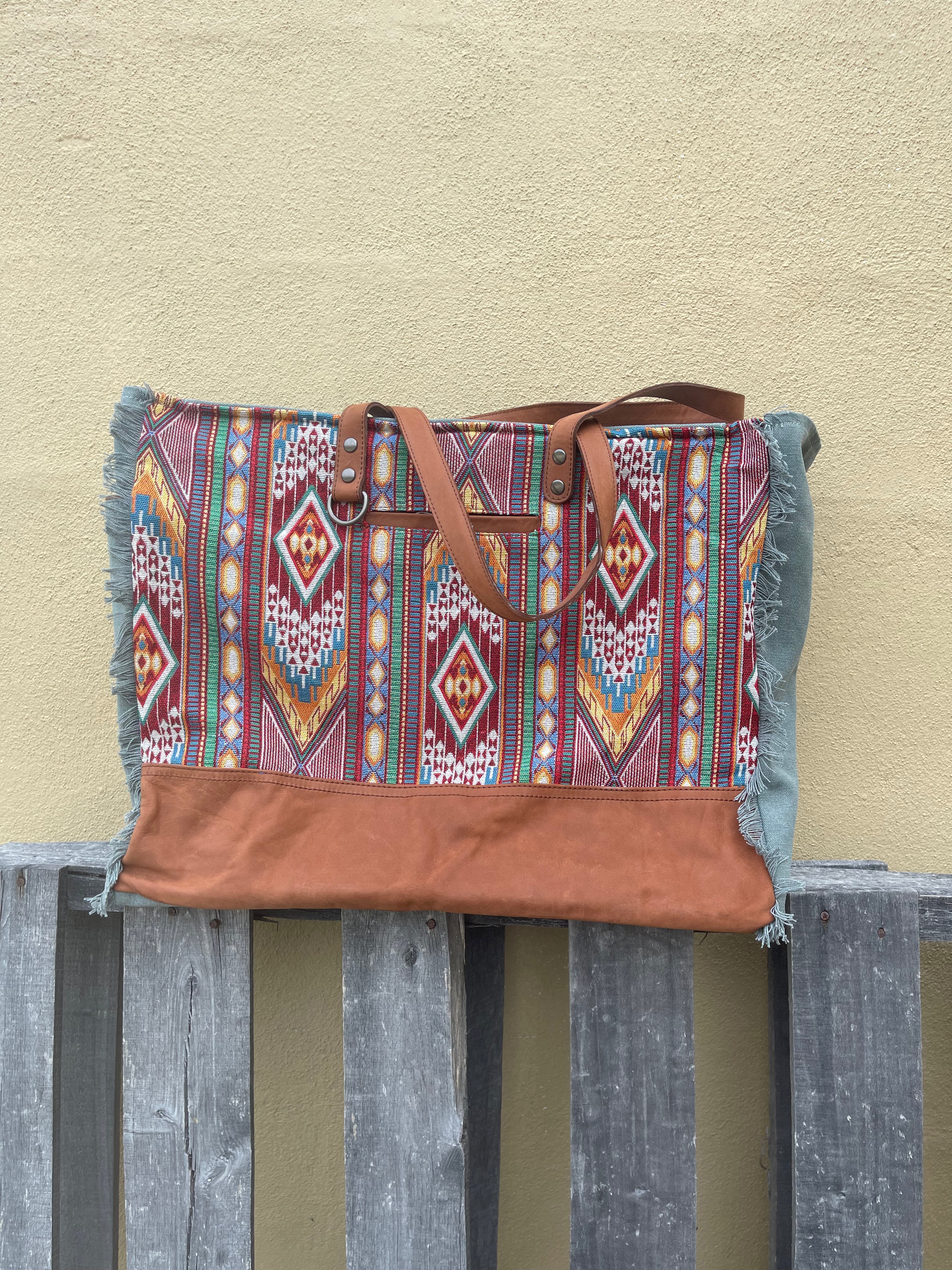 A red multi canvas and leather weekender bag with geometric patterns. Front view showing front pocket, keyring holder, and shoulder straps. 