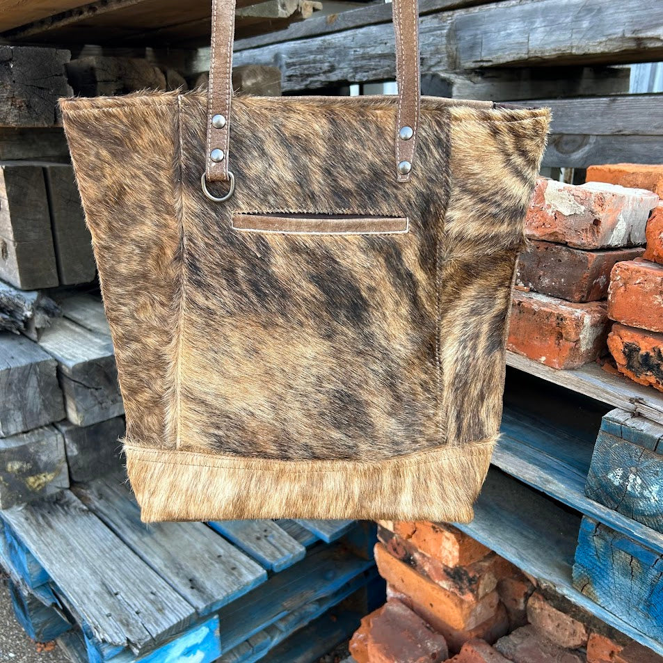 Brown leather and cowhide tote bag with a solid leather back with a concealed carry pocket. Close up view A