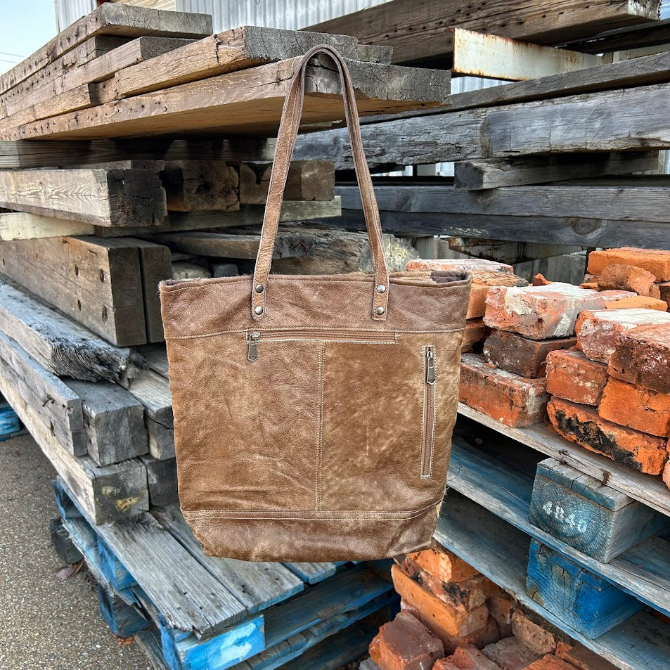 Brown leather tote bag on a background of stacked wooden planks and bricks