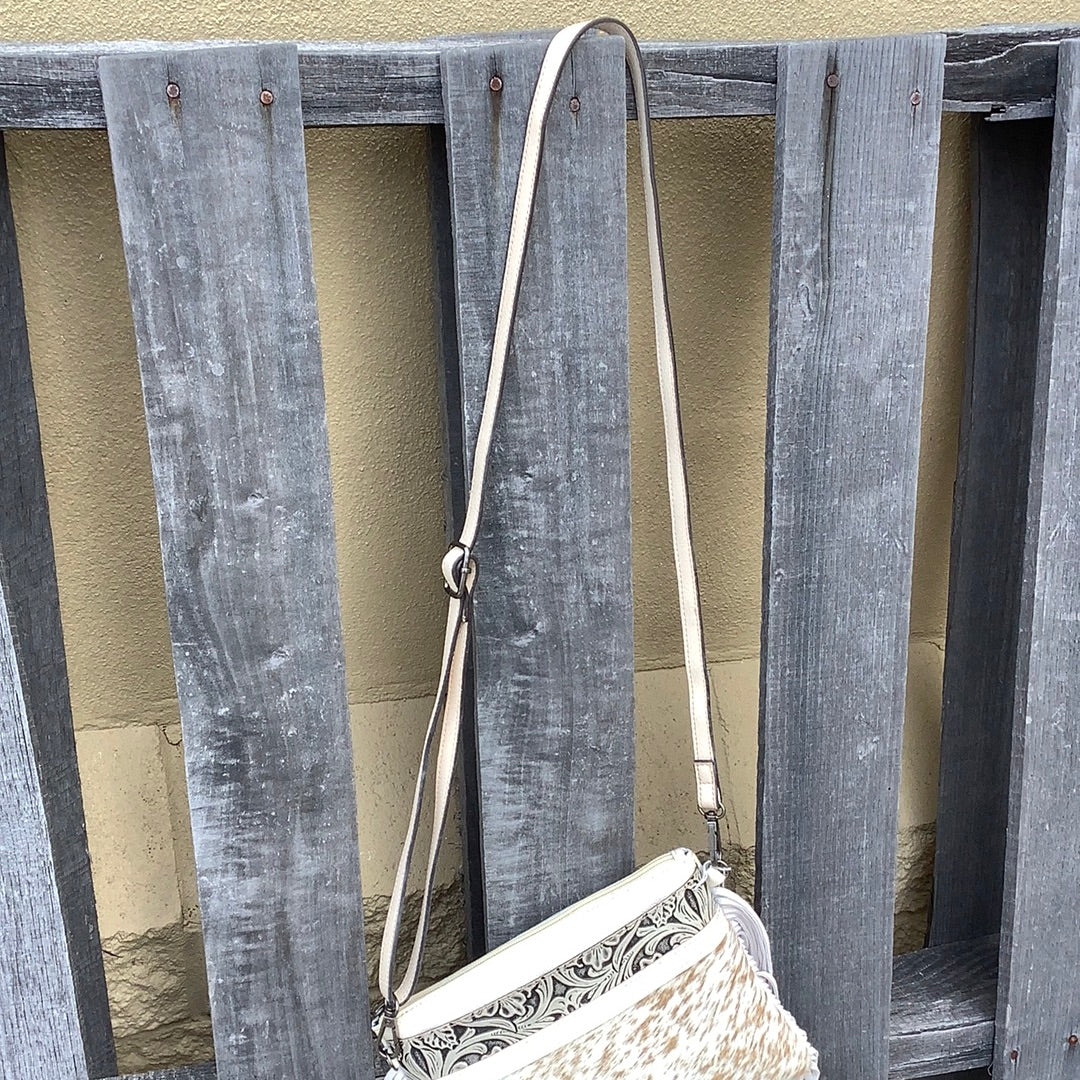 This cowhide and tooled leather crossbody bag features fringe sides and zips closed. The strap is removable and adjustable. View of crossbody strap. 