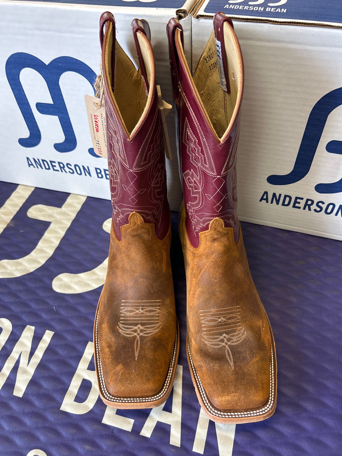 Pair of brown and maroon cowboy boots on a blue and white Anderson boot box background.
