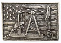 Metallic belt buckle with oil pumpjack, American flag, and tools on a wooden background