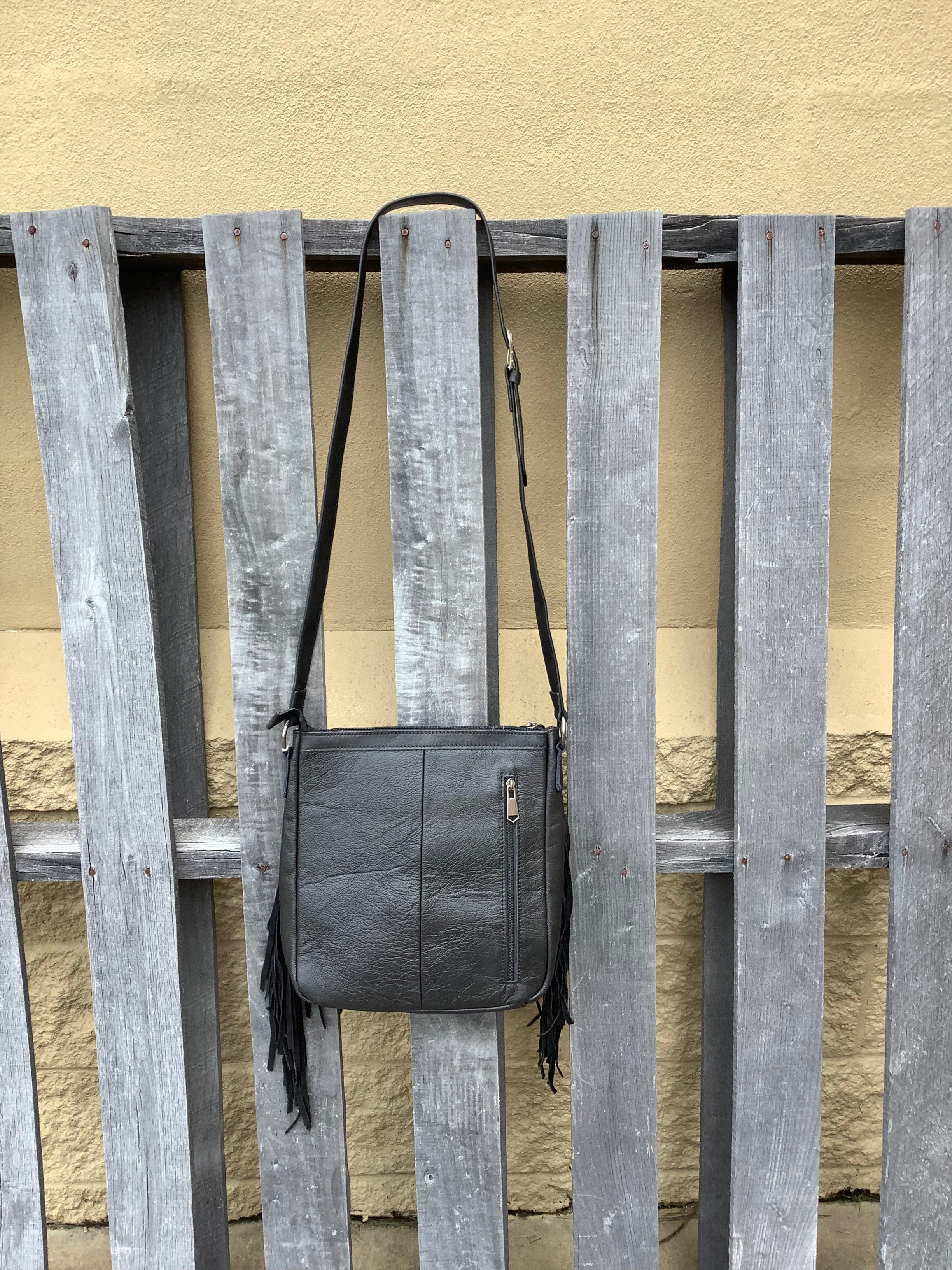 This Black leather and cowhide bag has side fringe and a tooled leather design. It has a rear concealed carry pocket. Rear view showing concealed carry pocket. 