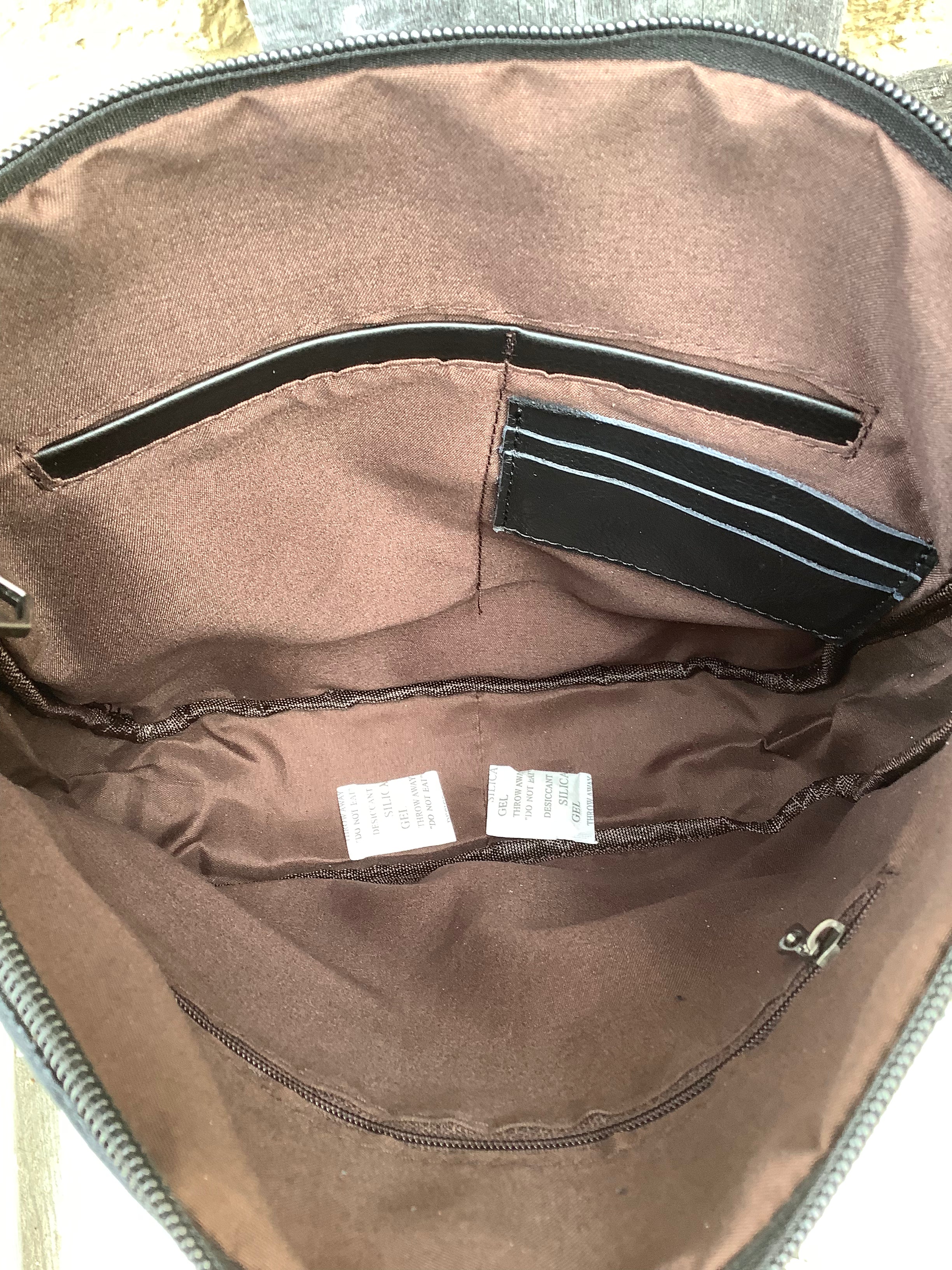 This Black leather and cowhide bag has side fringe and a tooled leather design. It has a rear concealed carry pocket. Inside view showing zippered close pocket and three credit card slots. 