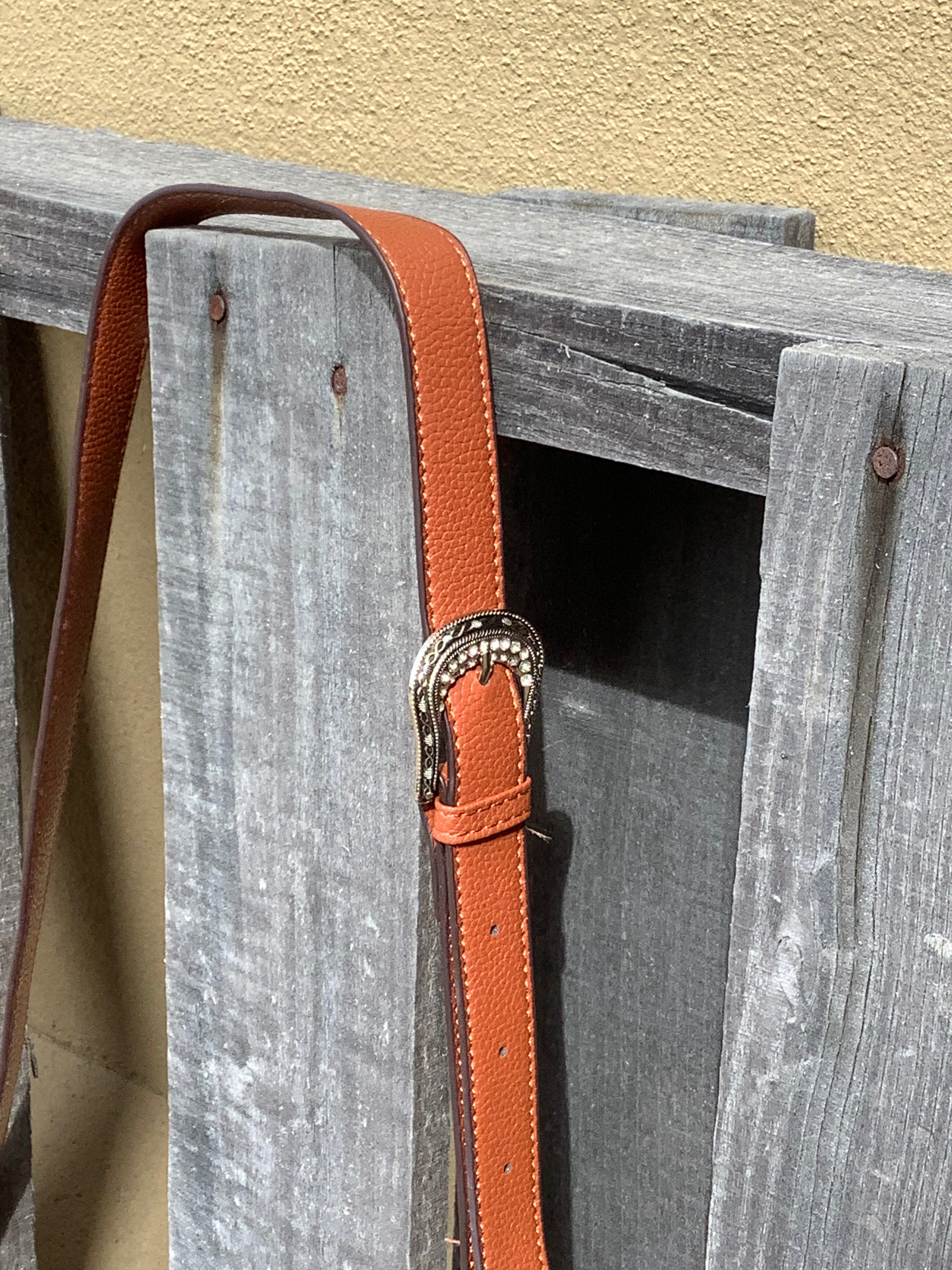 This Brown leather and cowhide shoulder bag has side fringe and a tooled leather design on the top. It has a rear concealed carry pocket. Close up view of strap showing adjustable buckle details. 