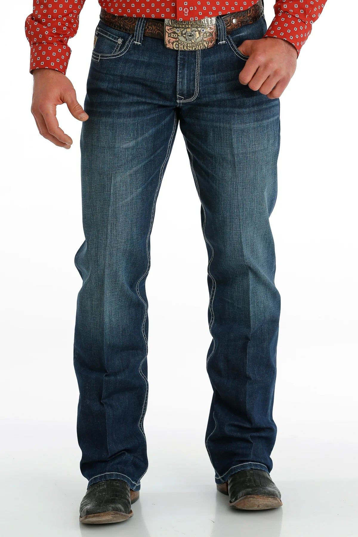 Men's Carter Medium Wash jeans front view showing whiskers, heavy sanding, and detail of front pockets and zipper. Also shows relaxed fit and boot cut stack on boots.