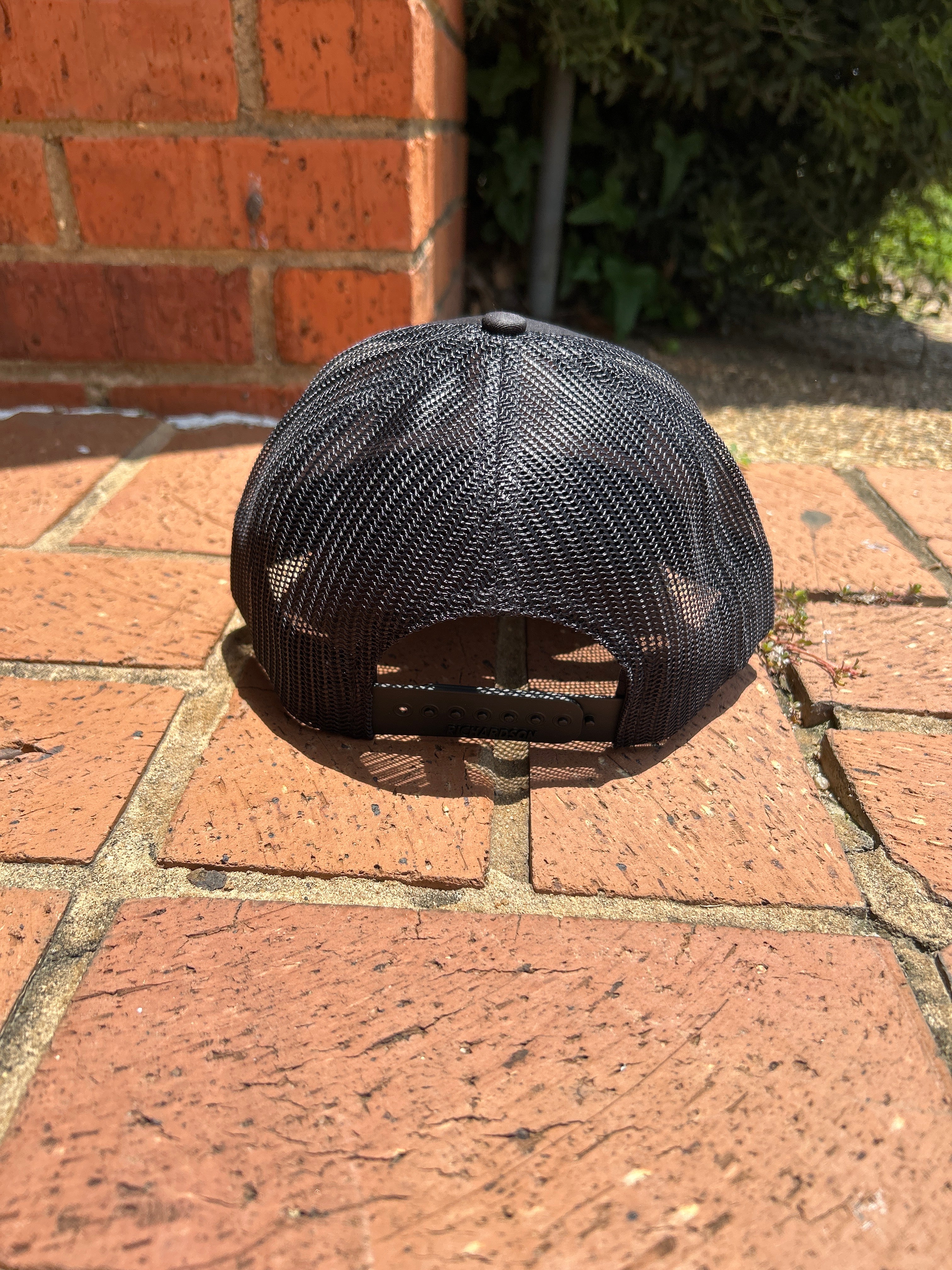 Back view of black mesh cap on a brick surface
