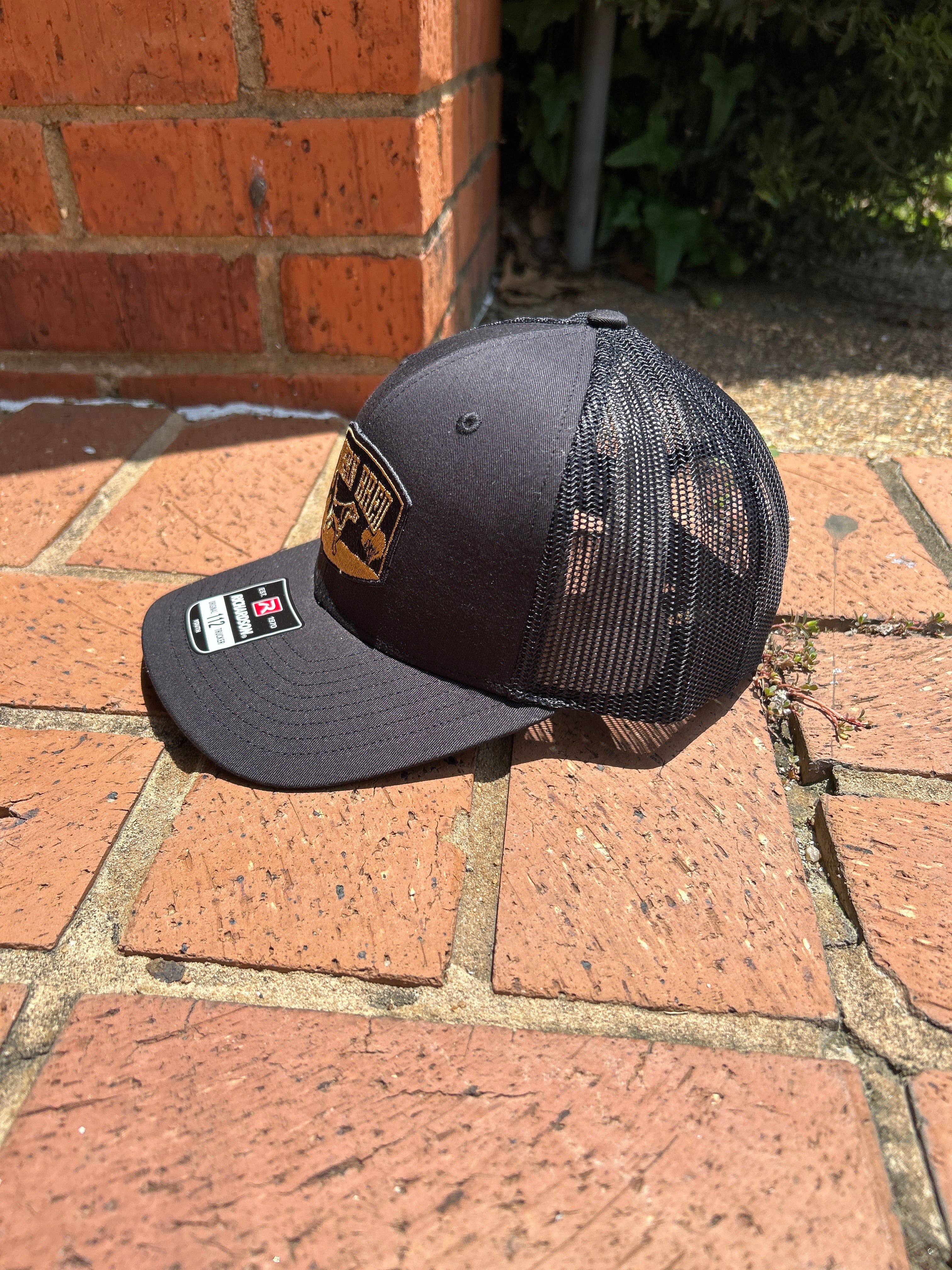 Side view of a black cap with a brand logo on a brick surface