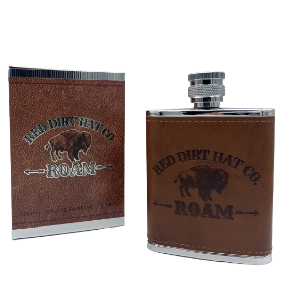 A bottle of Red Dirt Hat Company Roam cologne, with a brown leather-like wrap around the lower half and a metal cap. The bottle features the logo and the word 'ROAM' engraved on the front. It looks similar to a flask. 