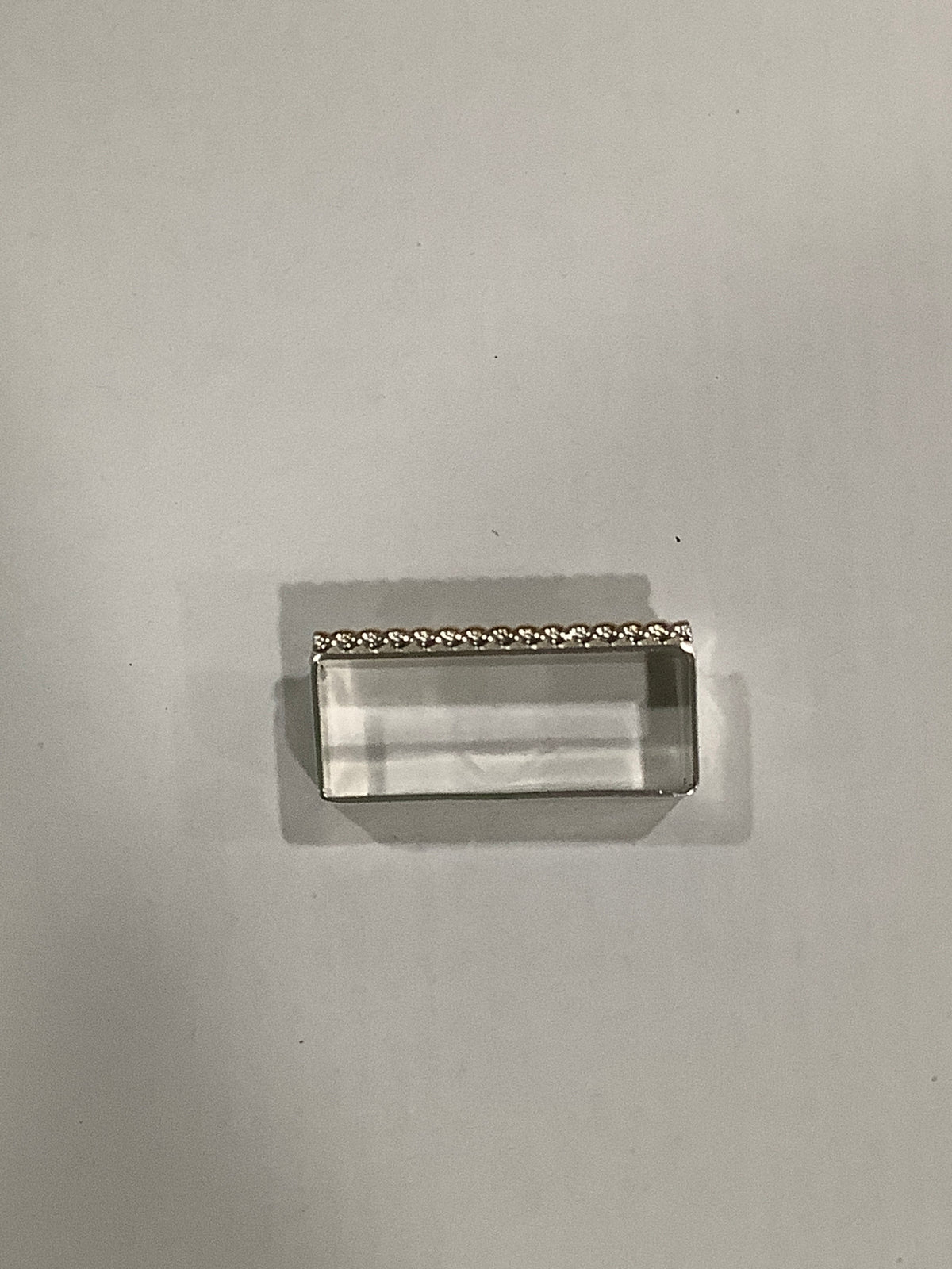 A small rectangular clear acrylic or glass block with a silver metal frame and a decorative beaded top edge, photographed on a plain light gray background.