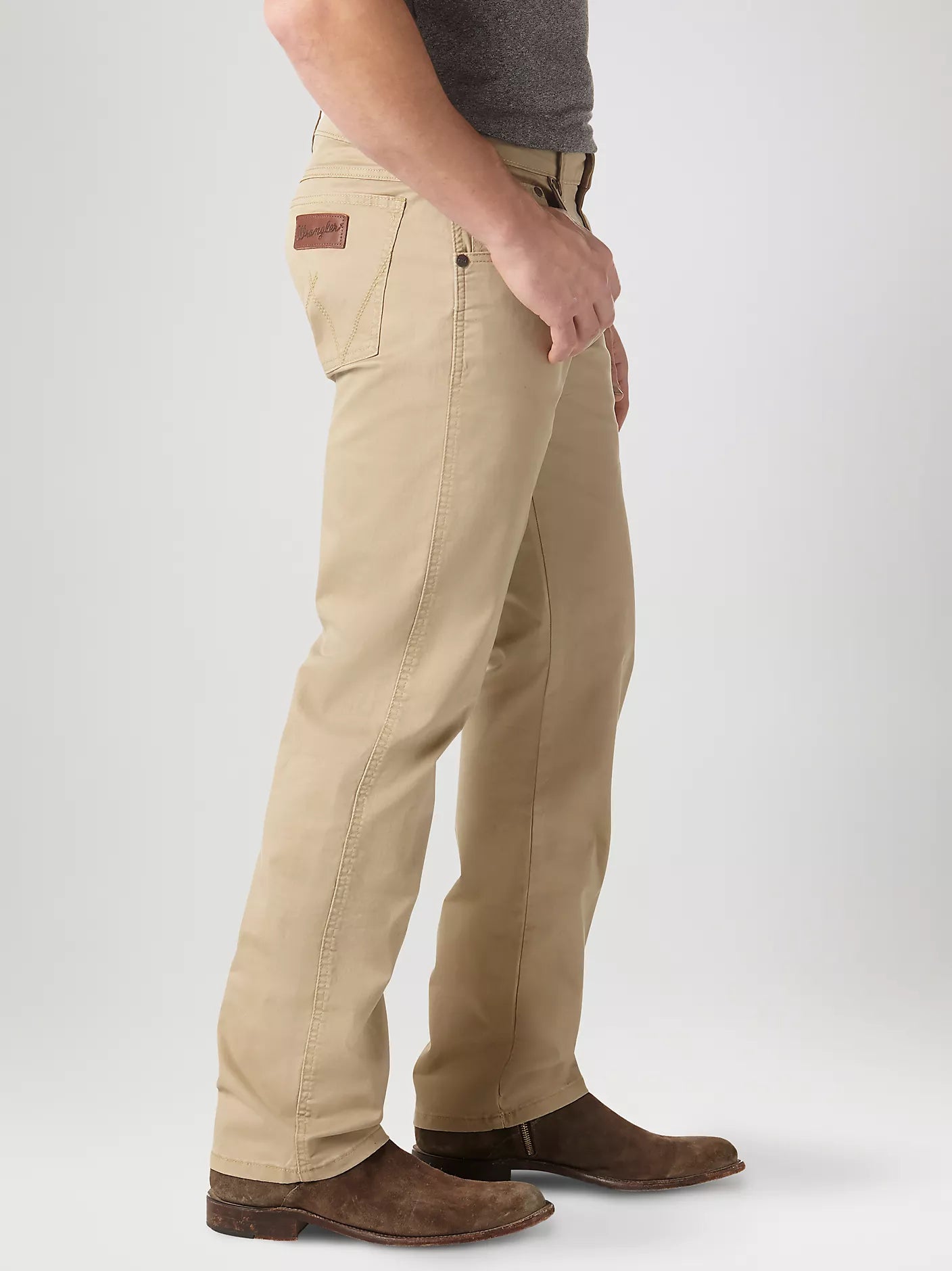 A man wearing Wrangler Retro men's fawn straight leg jeans with and boots. Side view shows brown neolite patch on right back pocket.
