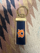 Front of AU ribbon key fob showing embroidered orange logo on blue ribbon sewn to burlap strap. Attached by brass finish metal connector to round key ring.