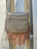 This Coffee Brown tooled leather crossbody bag has a turquoise inlay in the flap closure bordered with whip stitch. It has brown fringe, strap, and back. Rear view showing zip closure pocket. 