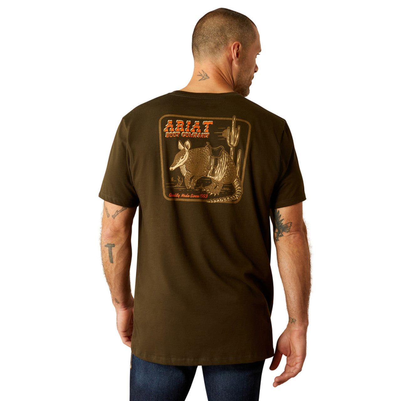 Men's Ariat short sleeve tee in Dark Olive with a armadillo graphic print on back. Rear view showing shirt untucked. 