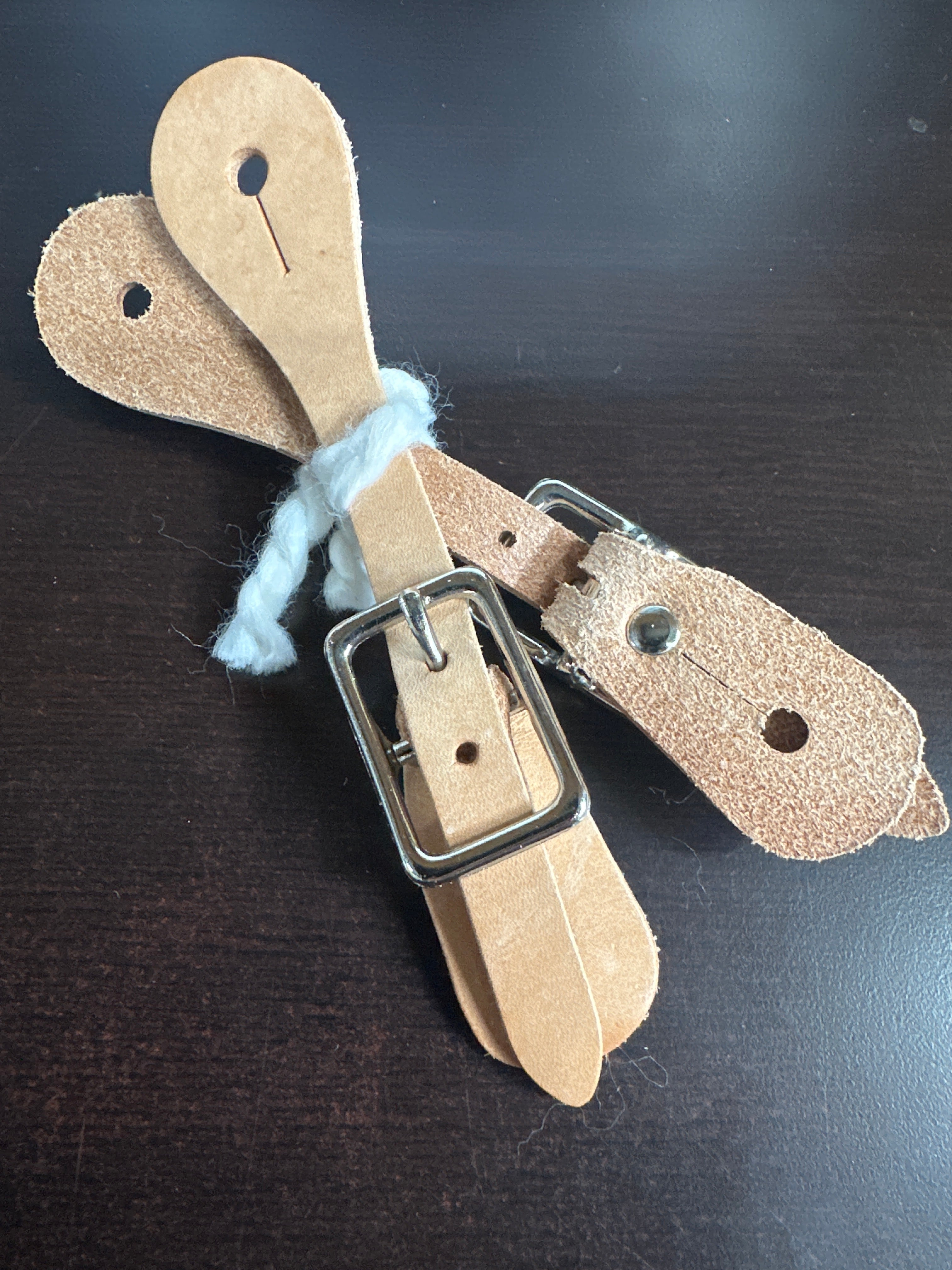 A pair of youth leather spur straps with natural color and metal buckles.