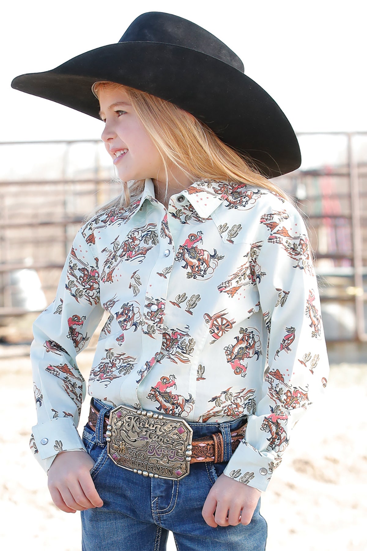 Young girl wearing a Cruel Denim pale blue printed snap Long Sleeve Western Shirt with a black cowboy hat, jeans and a belt. Front view.