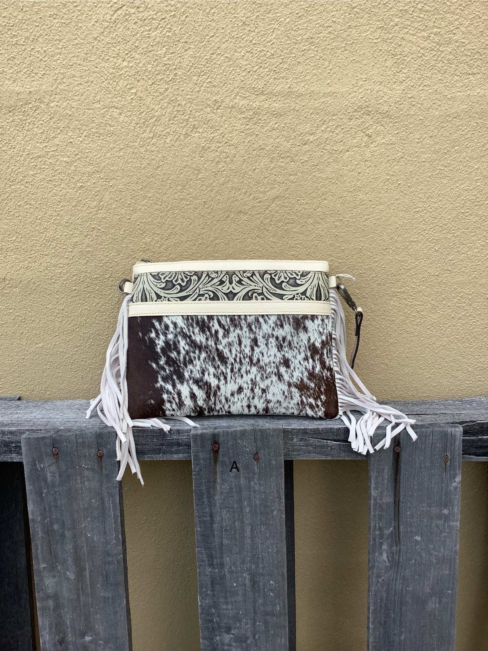 This cowhide and tooled leather crossbody bag features fringe sides and zips closed. The strap is removable and adjustable. Front View A