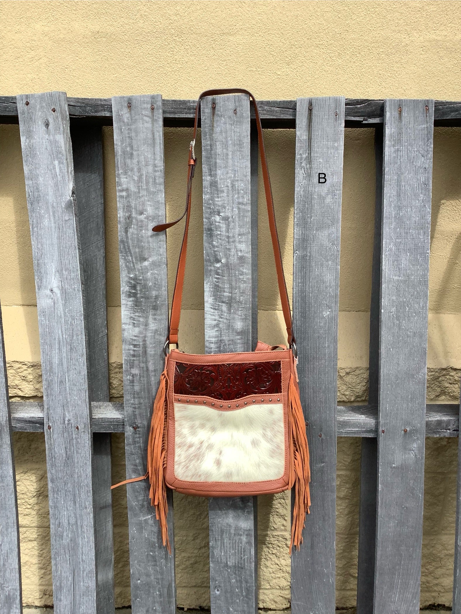 This Brown leather and cowhide shoulder bag has side fringe and a tooled leather design on the top. It has a rear concealed carry pocket. Front View B