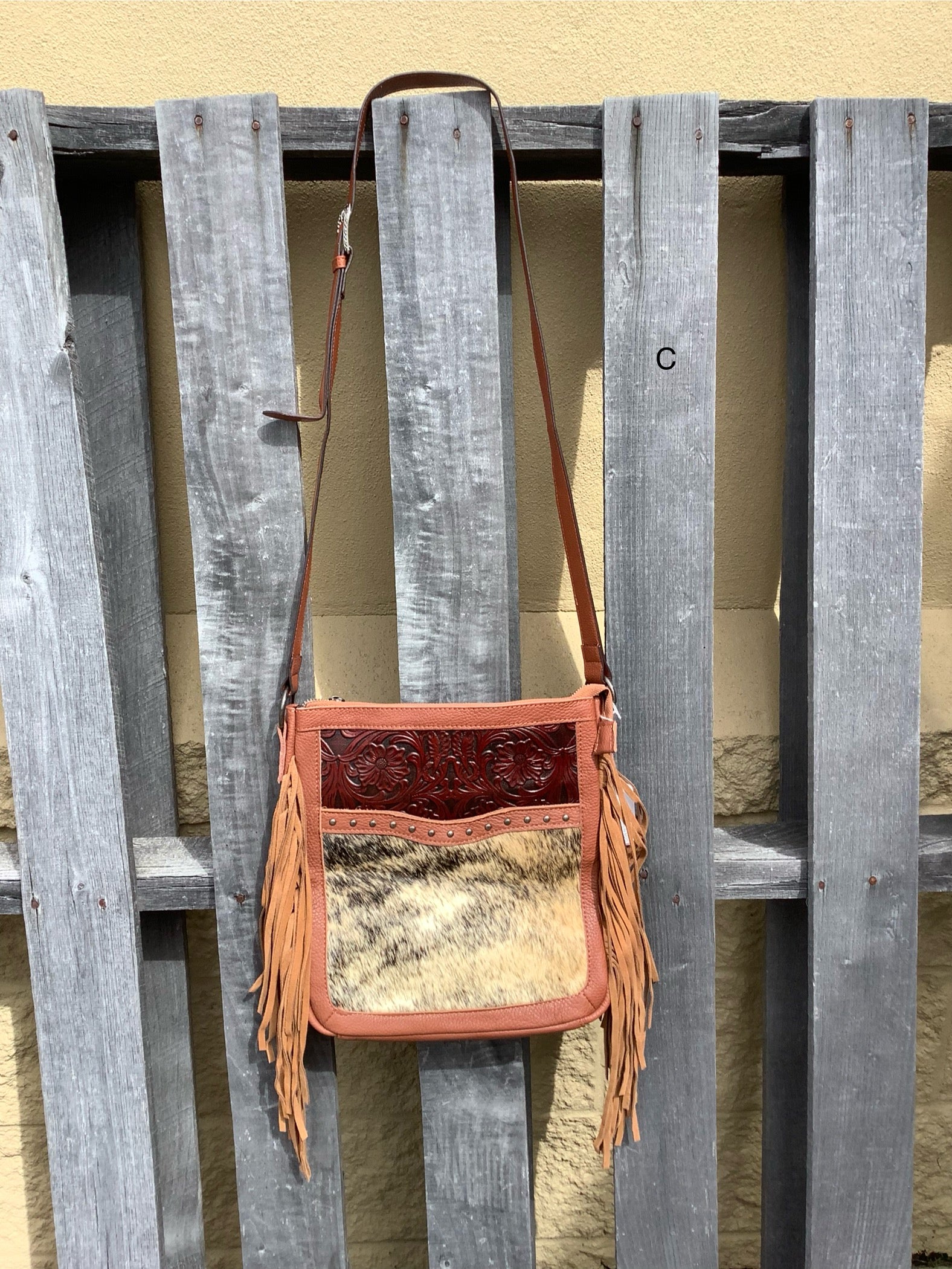 This Brown leather and cowhide shoulder bag has side fringe and a tooled leather design on the top. It has a rear concealed carry pocket. Front View C