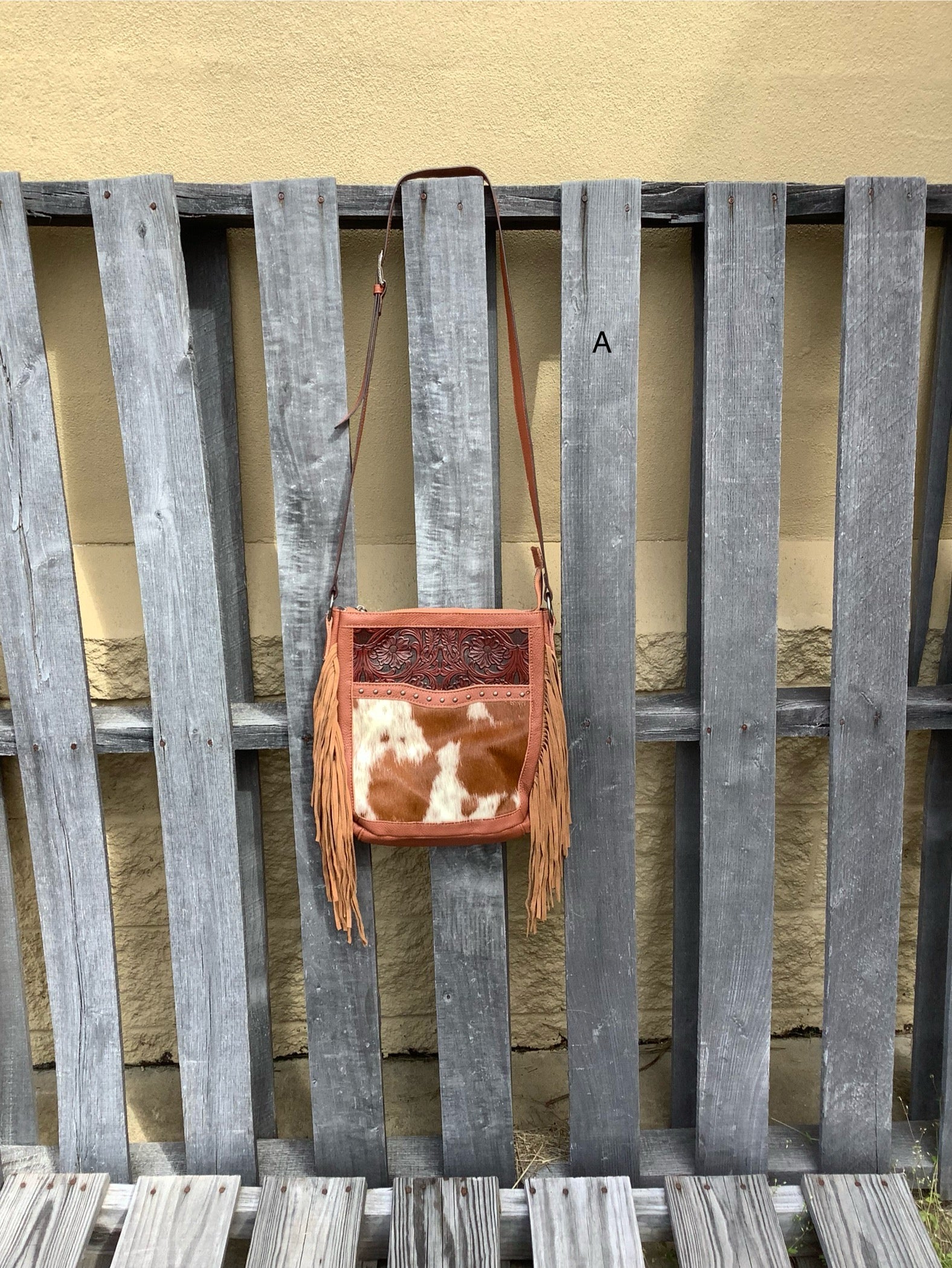 This Brown leather and cowhide shoulder bag has side fringe and a tooled leather design on the top. It has a rear concealed carry pocket. Front View A