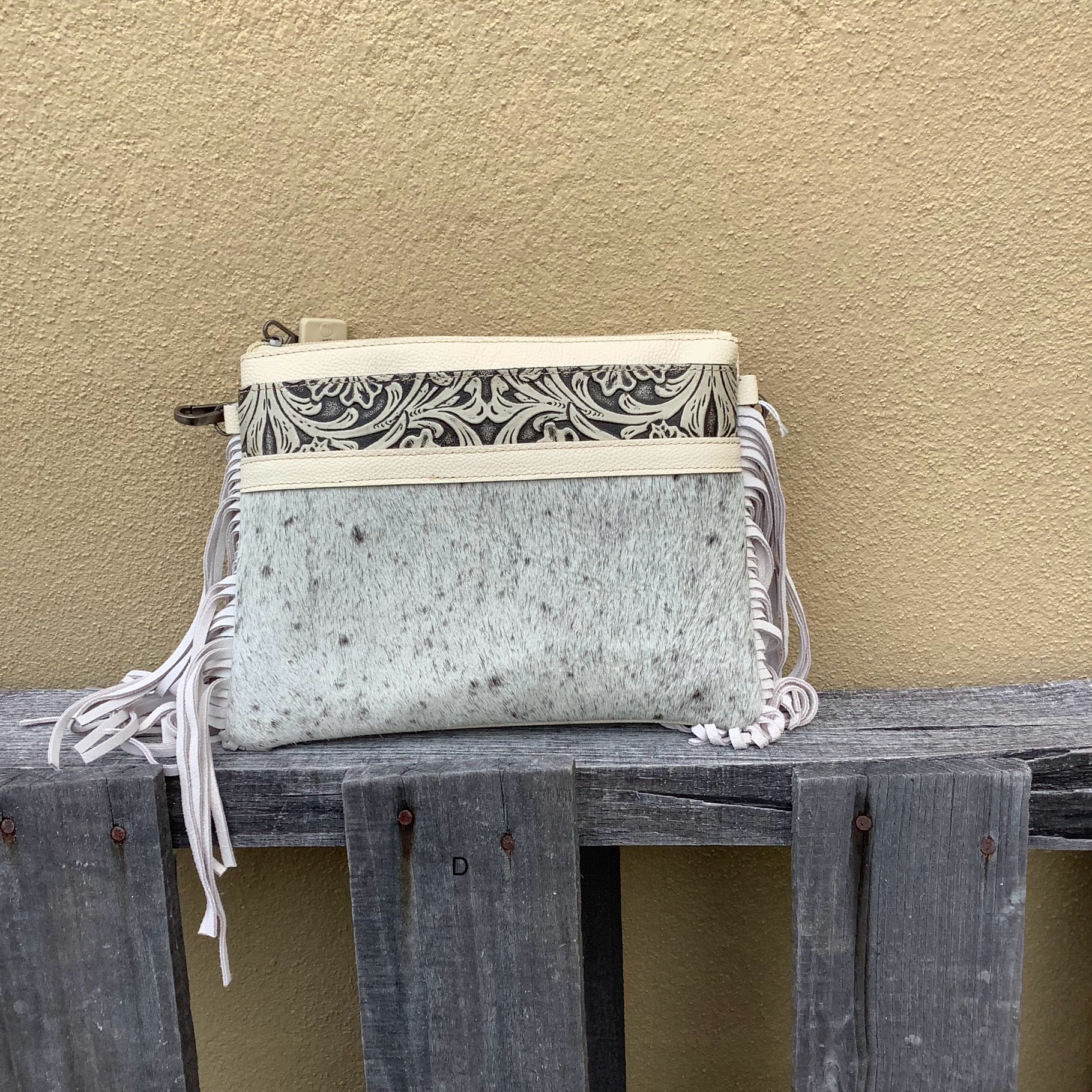 This cowhide and tooled leather crossbody bag features fringe sides and zips closed. The strap is removable and adjustable.  Front View D