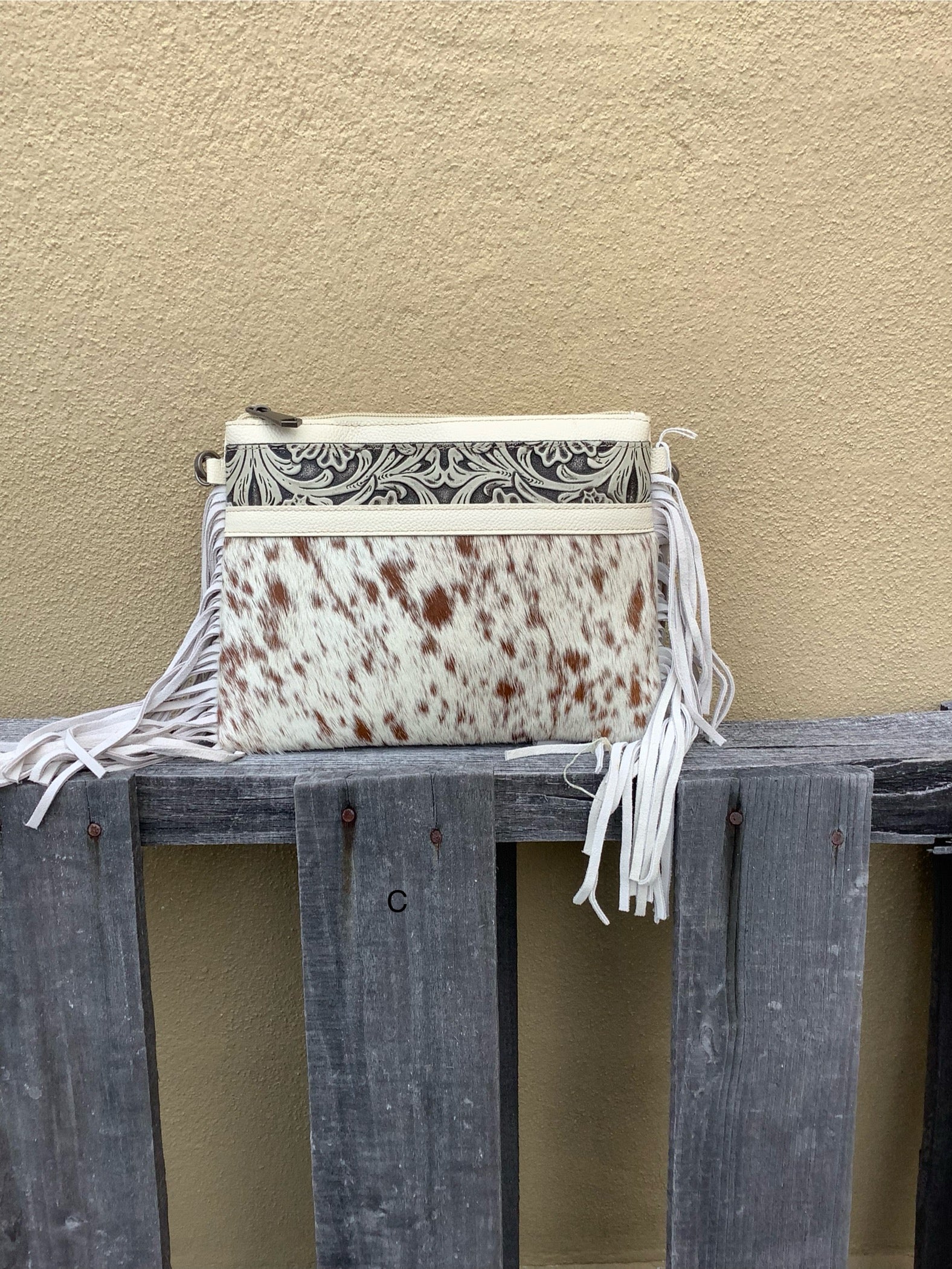 This cowhide and tooled leather crossbody bag features fringe sides and zips closed. The strap is removable and adjustable. Front View C