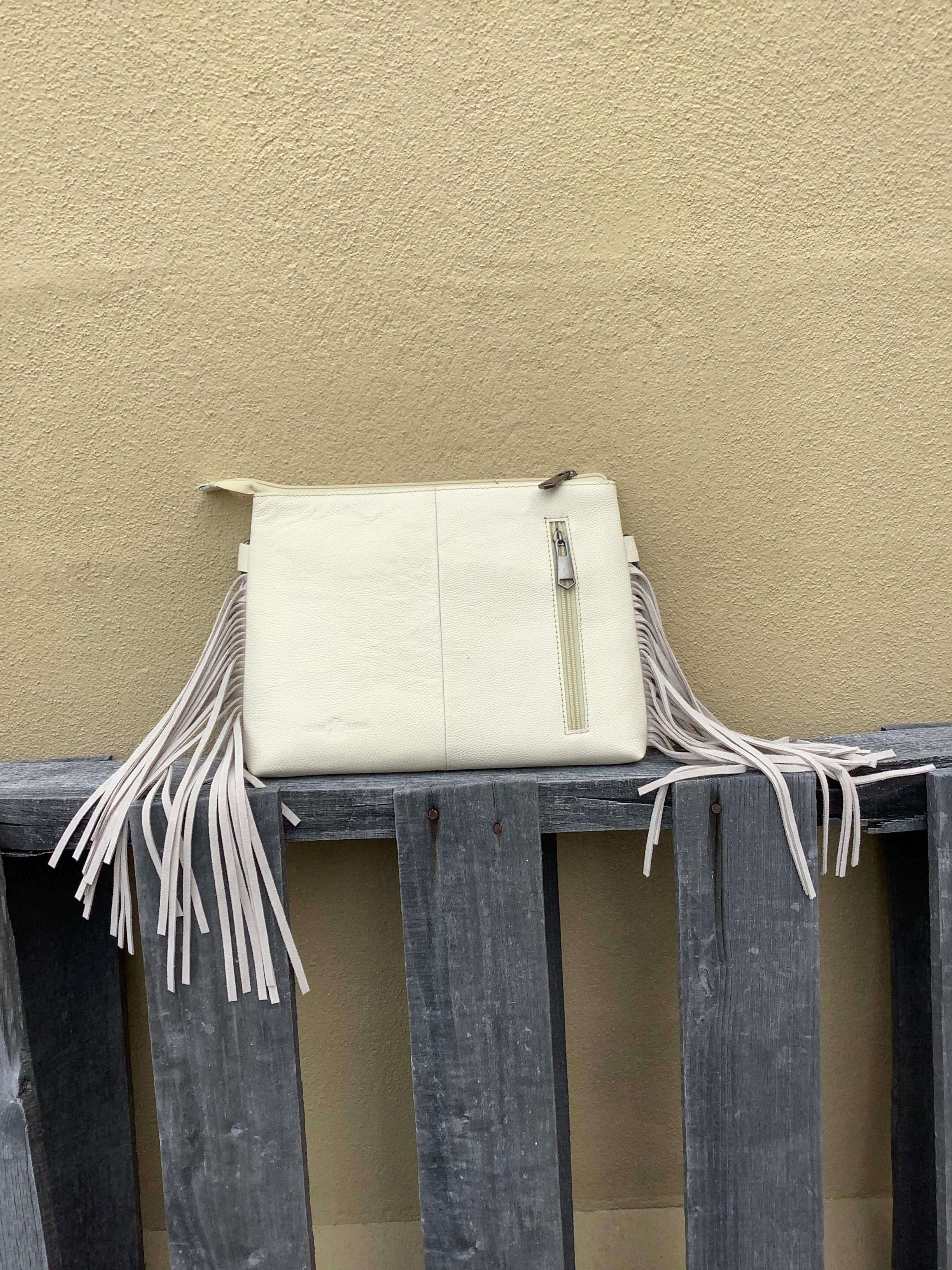 Beige tooled leather and cowhide purse with fringe details and a zippered closure. Rear view showing concealed carry pocket.