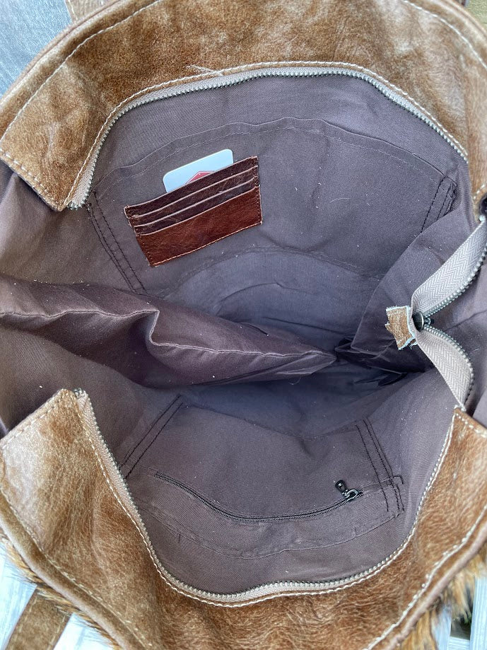 Brown leather and cowhide tote bag with a solid leather back with a concealed carry pocket. Inside view showing three credit card slots, zippered close pocket, and two additional pockets. 