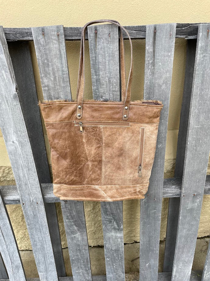 Brown leather and cowhide tote bag with a solid leather back with a concealed carry pocket. Rear view showing the solid brown leather back with concealed carry pocket and a zippered closed pocket. 