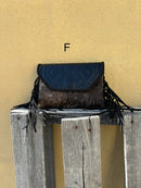 This cowhide and black leather crossbody bag has fringe sides. It features a whipstitch flap closure with a geometric design. Front View F