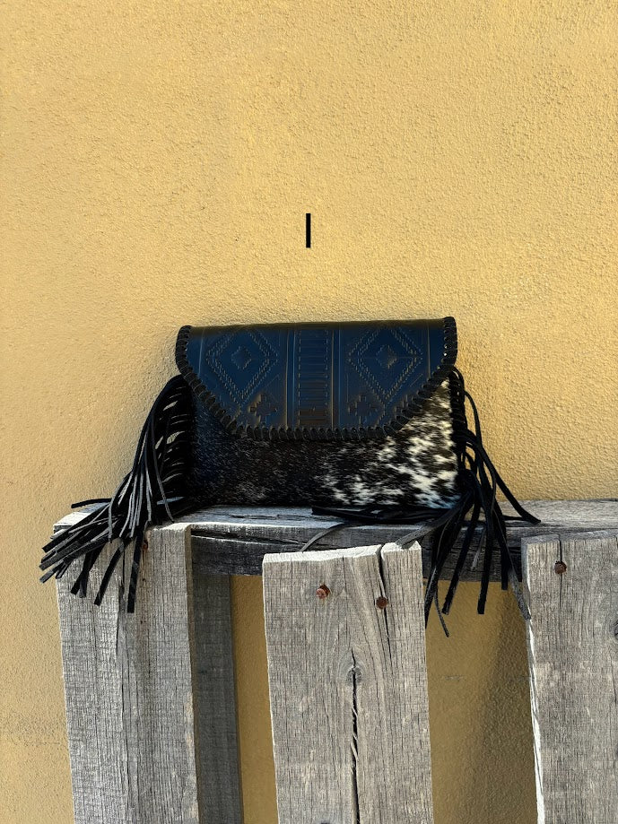 This cowhide and black leather crossbody bag has fringe sides. It features a whipstitch flap closure with a geometric design. Front View I